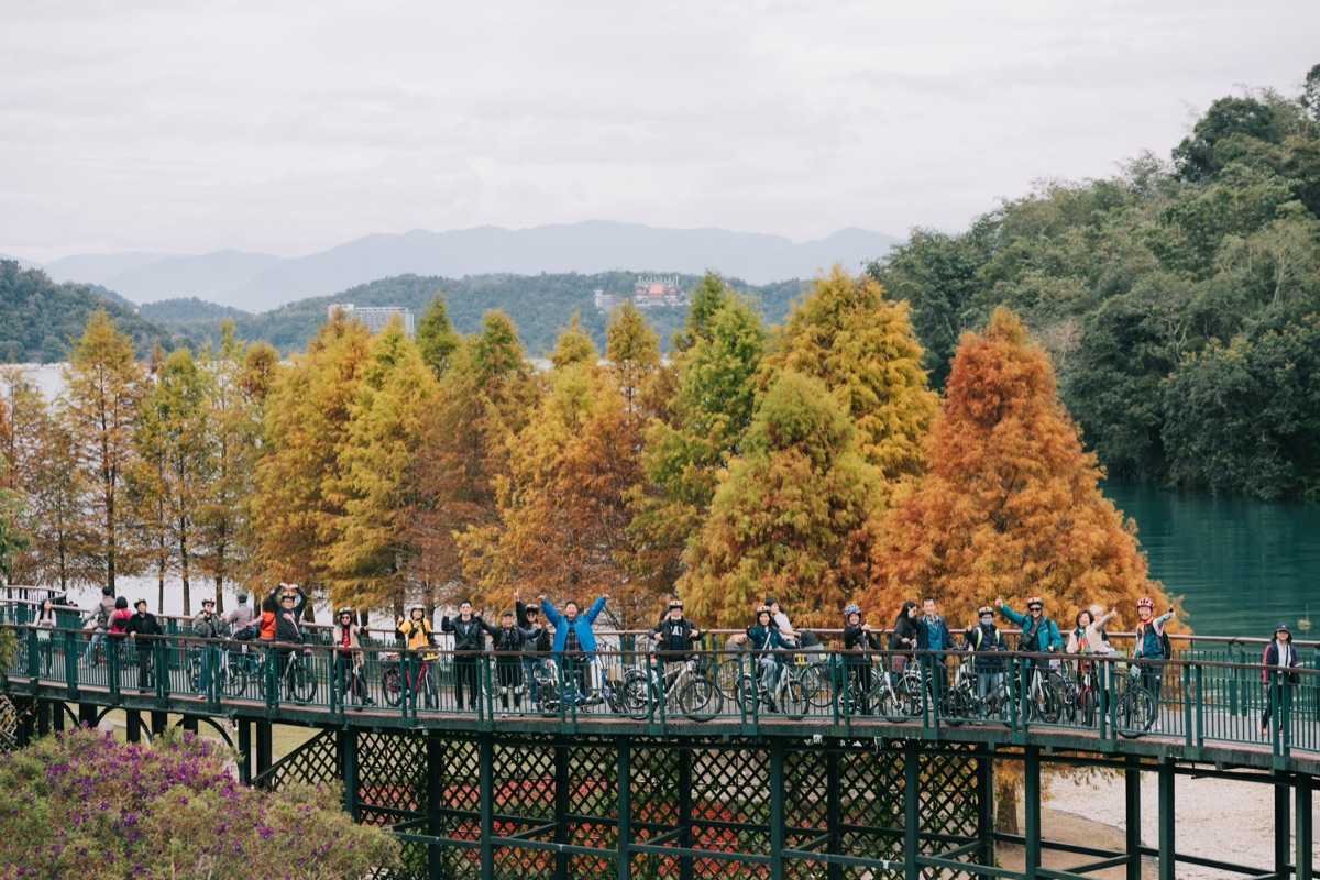 Group of cyclists posing on the iconic green bridge at Sun Moon Lake with autumn foliage