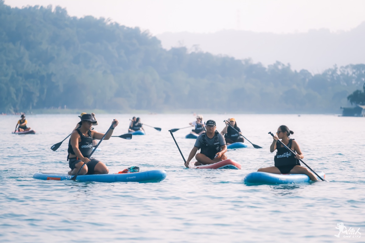Group SUP paddleboarding on Sun Moon Lake at sunrise with misty mountains
