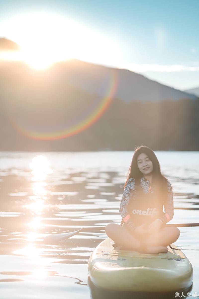 Woman meditating on SUP board at sunrise on Sun Moon Lake with golden light